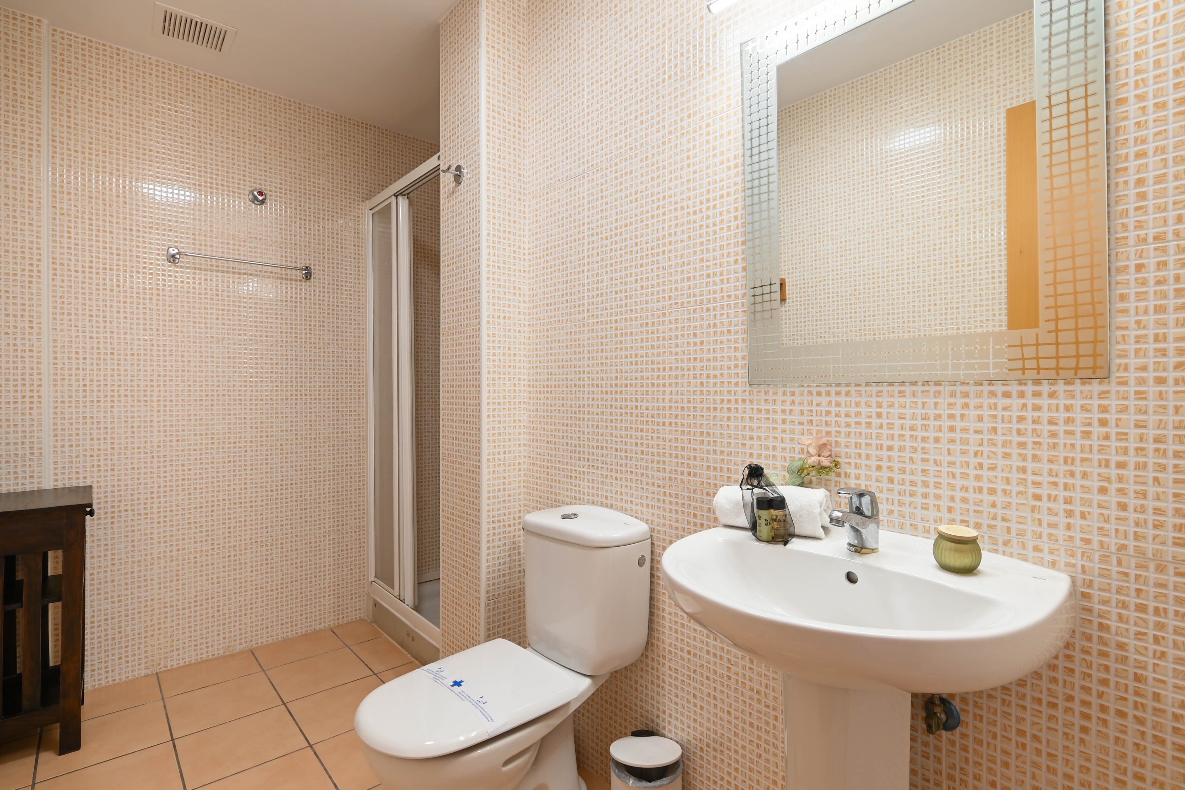Functional bathroom featuring beige mosaic wall tiles, a white pedestal sink, and a walk-in shower with a folding glass door.