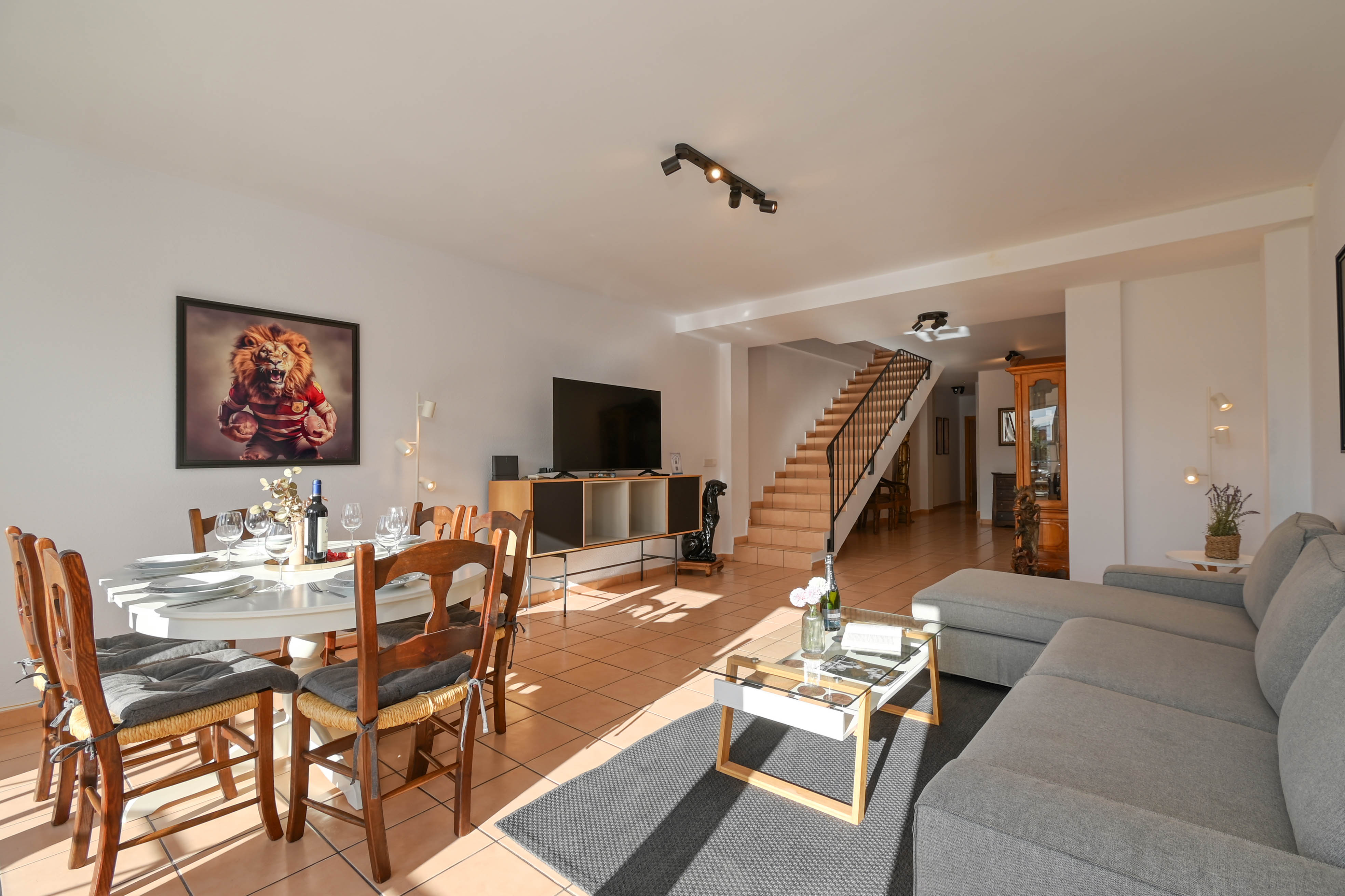 Open-plan living area featuring terracotta flooring, a grey sectional sofa, and a staircase leading to the upper floor of the duplex apartment.