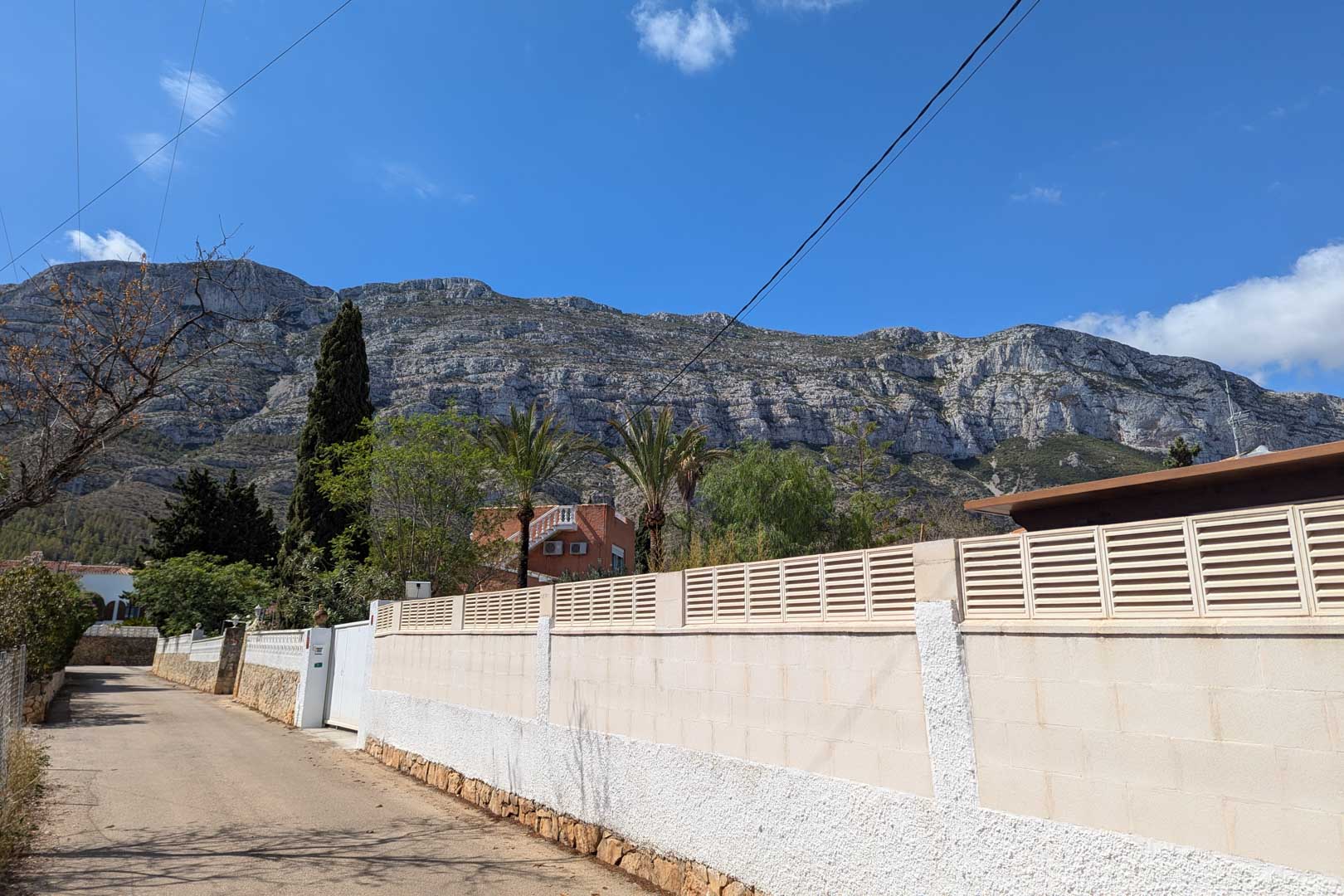 Exterior street view featuring the property's perimeter wall set against the dramatic limestone cliffs of the Montgó mountain range.
