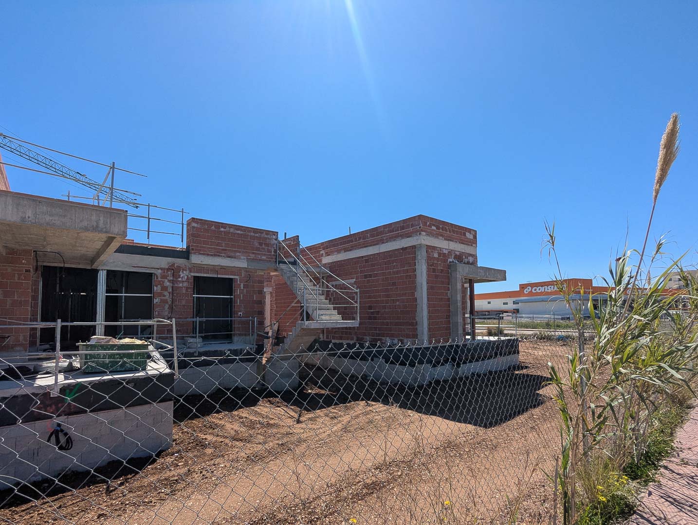 Exterior view of the villa under construction, featuring the red brick structure, concrete stairs, and its convenient location near local commercial services.