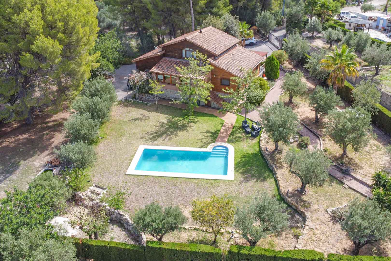 Aerial view of the Finnish pine villa and private pool, showcasing the stone-clad base and Mediterranean gardens with olive trees in Orba, Alicante.