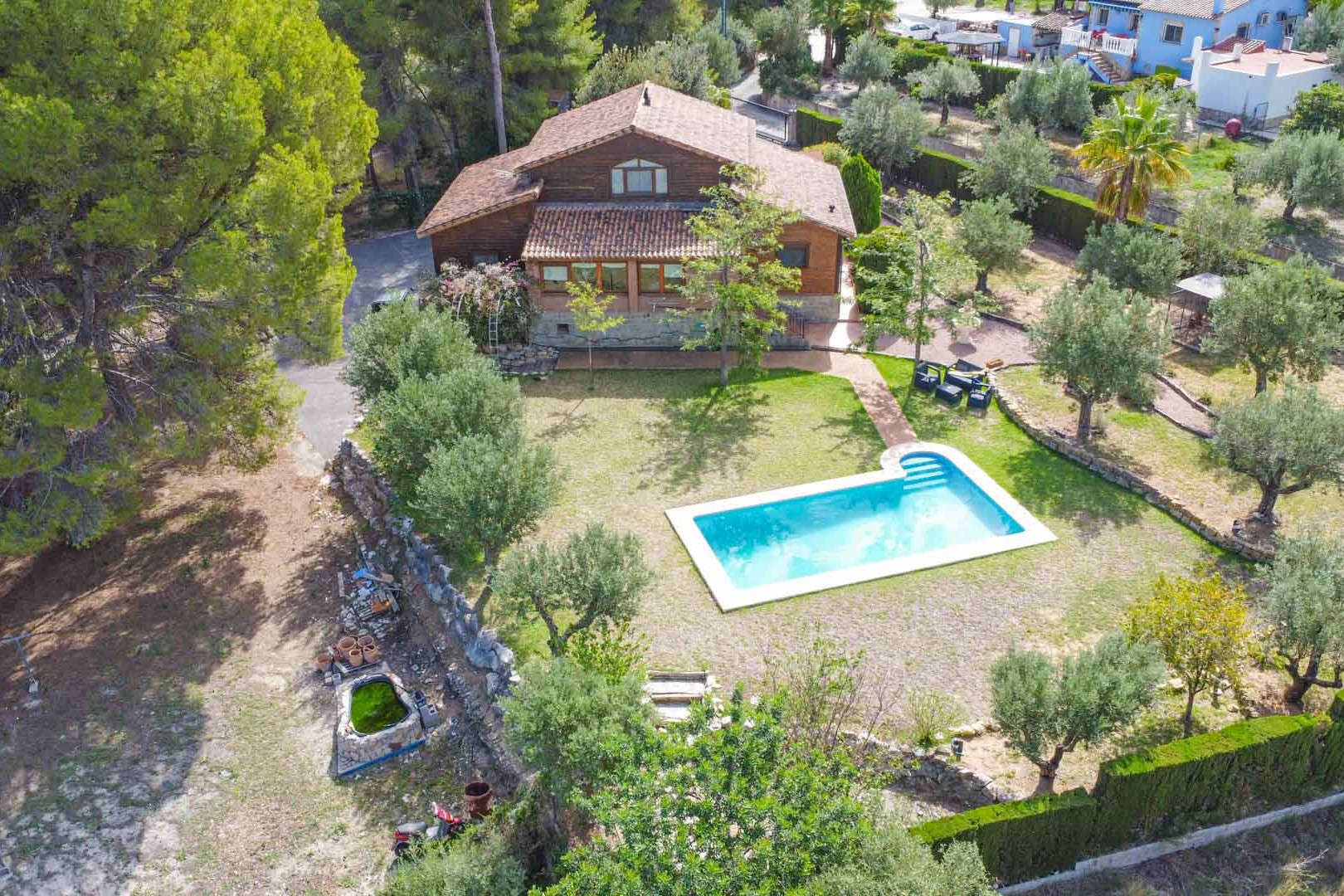 Aerial view of the Finnish pine villa featuring a private swimming pool, manicured lawn, and Mediterranean gardens with olive trees in Orba.