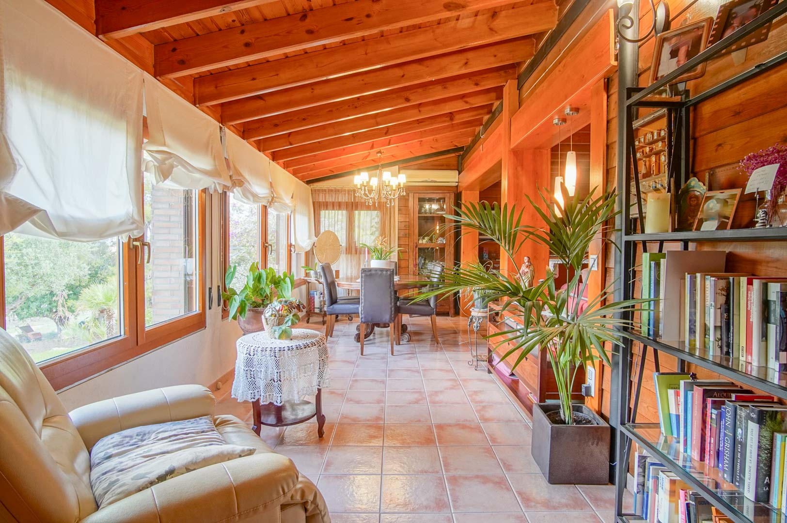 Bright sunroom featuring Finnish pine beam ceilings, terracotta flooring, and large windows with garden views, integrating a cozy reading nook and dining area.