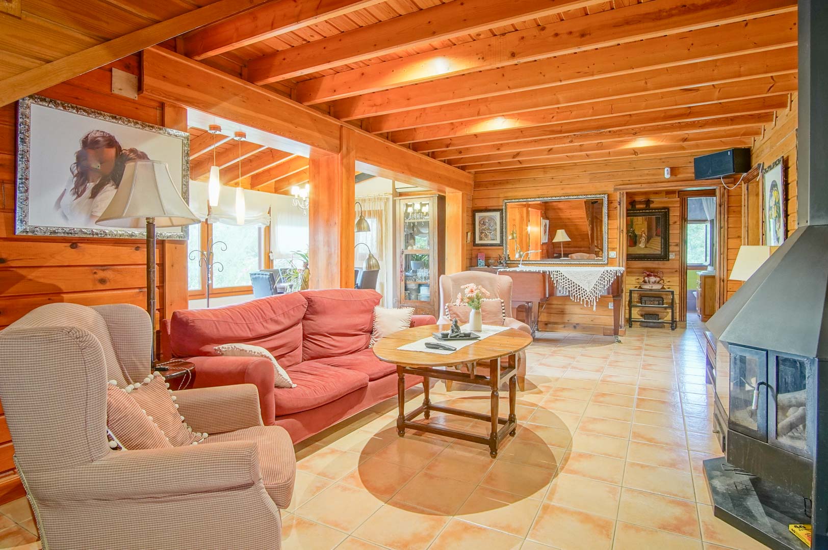 Cozy living room featuring Finnish pine walls, exposed ceiling beams, and a central fireplace. The space is defined by terracotta-style flooring and natural wood textures.
