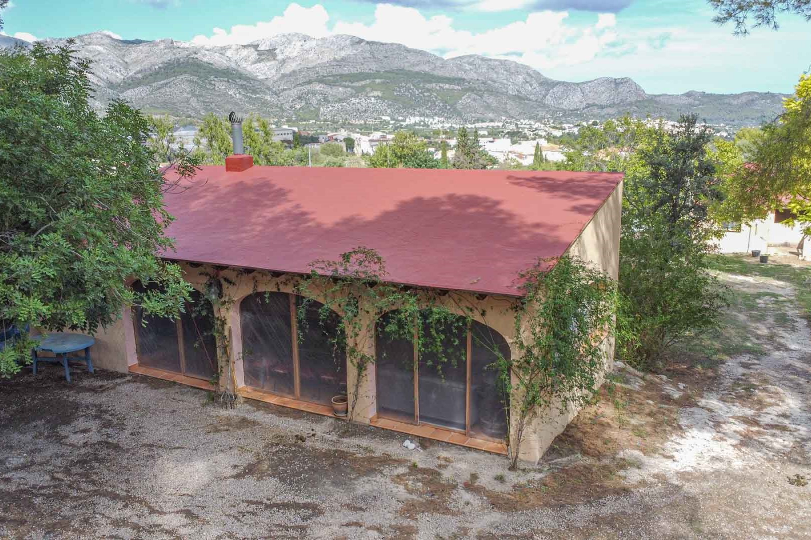 Exterior view of the detached outbuilding featuring arched glass doors and a chimney, set against a backdrop of the Orba valley and surrounding mountains.