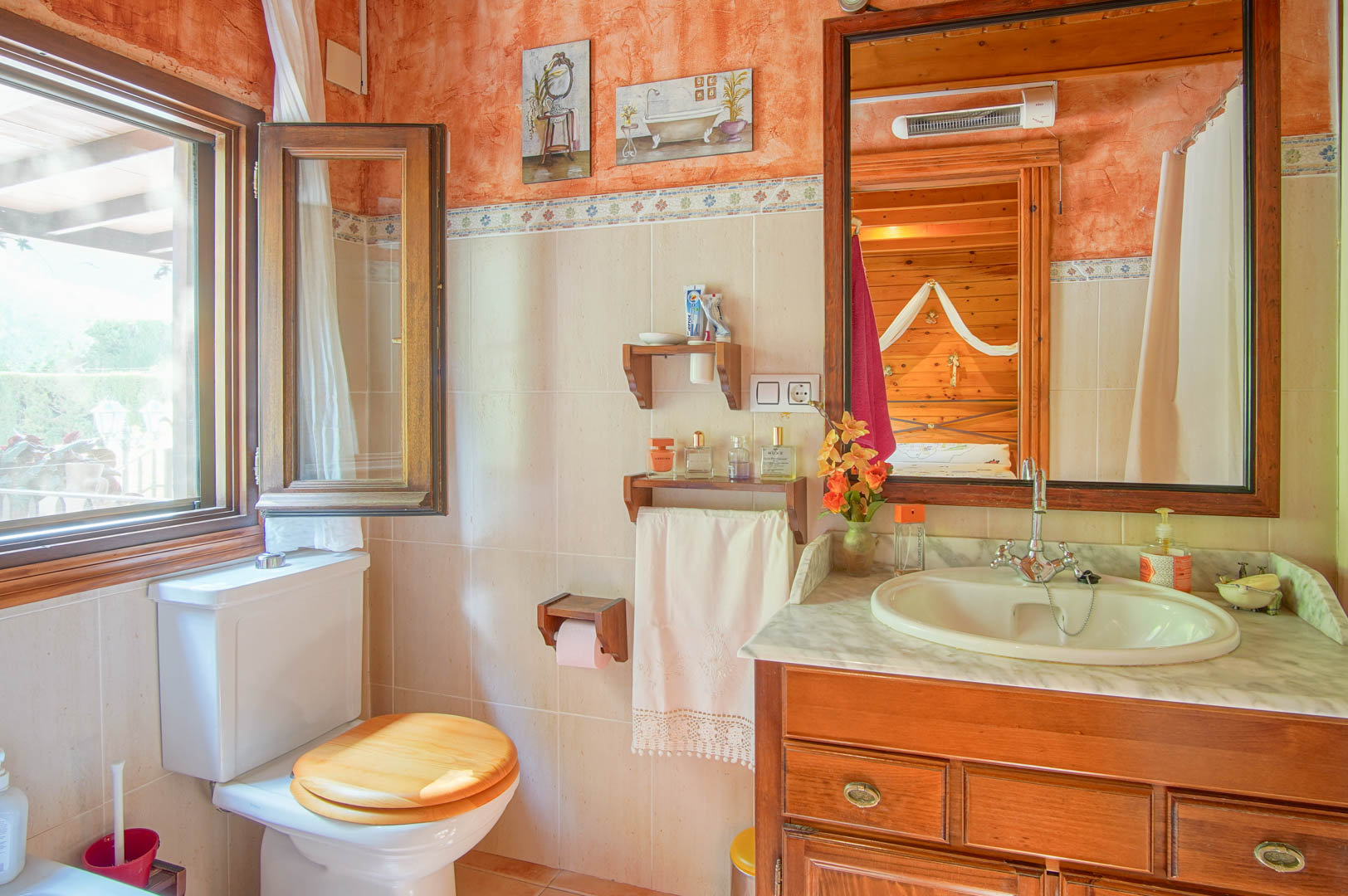 Rustic bathroom featuring a wooden vanity with a marble countertop and an open window. The mirror reflects the adjacent pine-paneled bedroom.