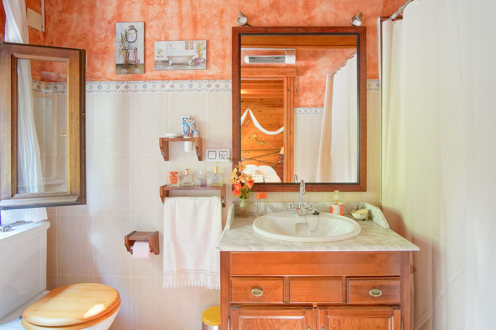 Rustic bathroom featuring a wooden vanity with a marble countertop, terracotta-textured walls, and a large mirror reflecting the pine-paneled bedroom interior.