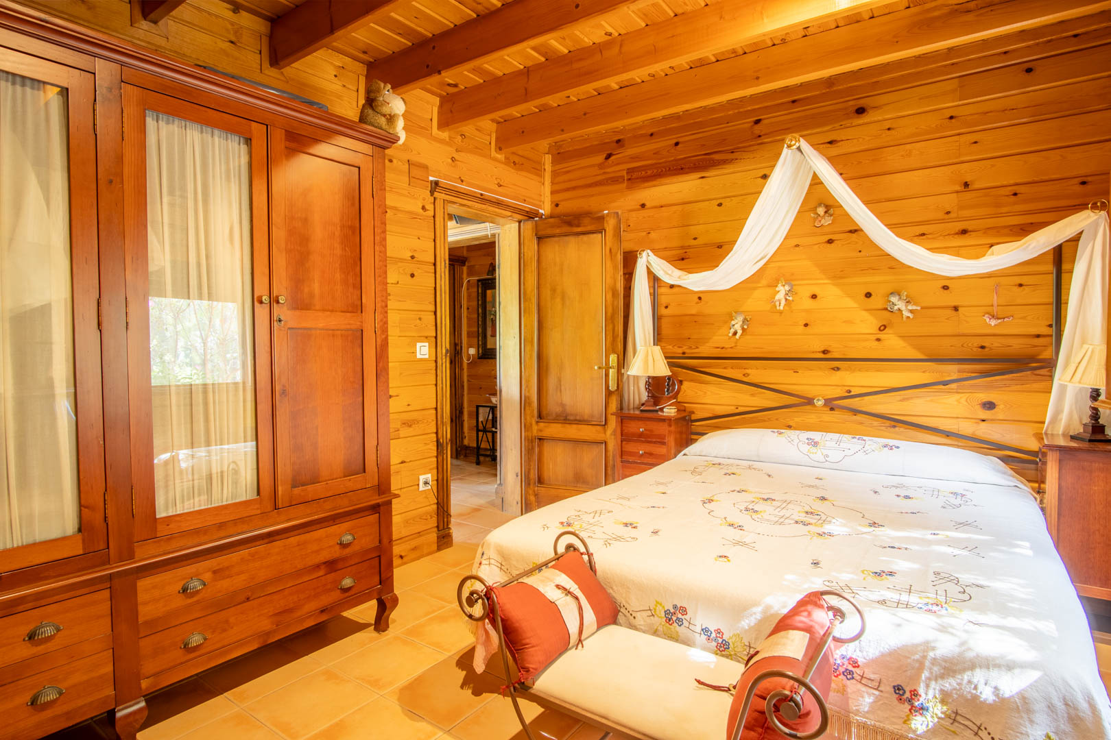 Rustic bedroom featuring Finnish pine walls and ceilings, a solid wood wardrobe, and a double bed with a decorative canopy and wrought iron headboard.