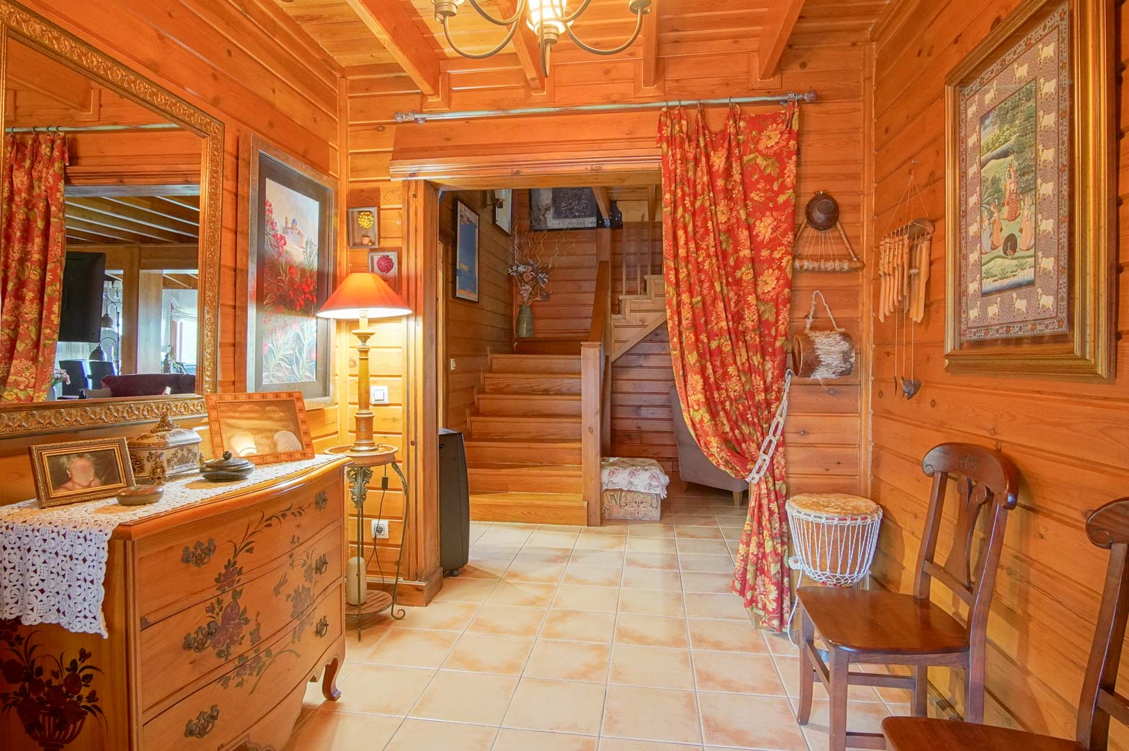 Rustic entrance hall featuring Finnish pine walls, ceramic flooring, and a wooden staircase. The space is decorated with traditional furniture and warm ambient lighting.