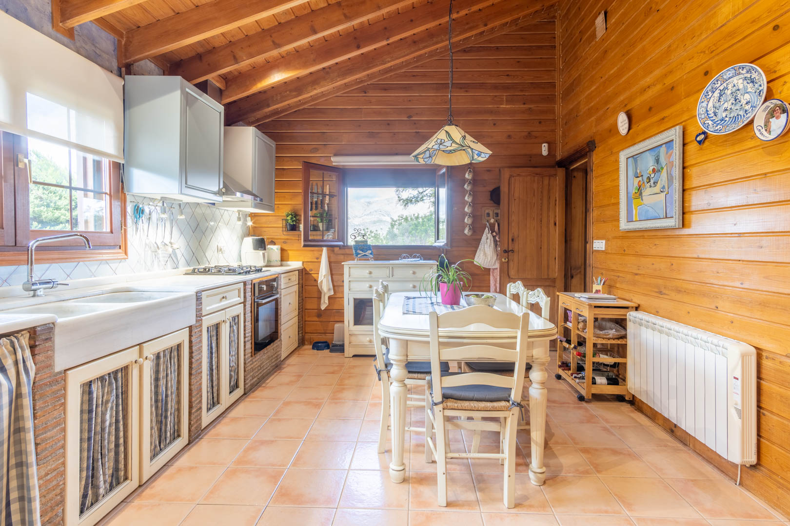 Rustic kitchen featuring Finnish pine walls and ceilings, brick-accented cabinetry, a marble sink, and a central dining area with mountain views.