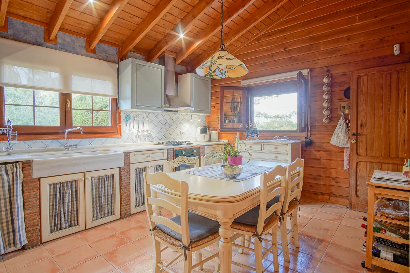 Rustic kitchen featuring Finnish pine walls, exposed brick cabinetry, and a marble sink. The space includes a central dining area and high ceilings with wooden beams.