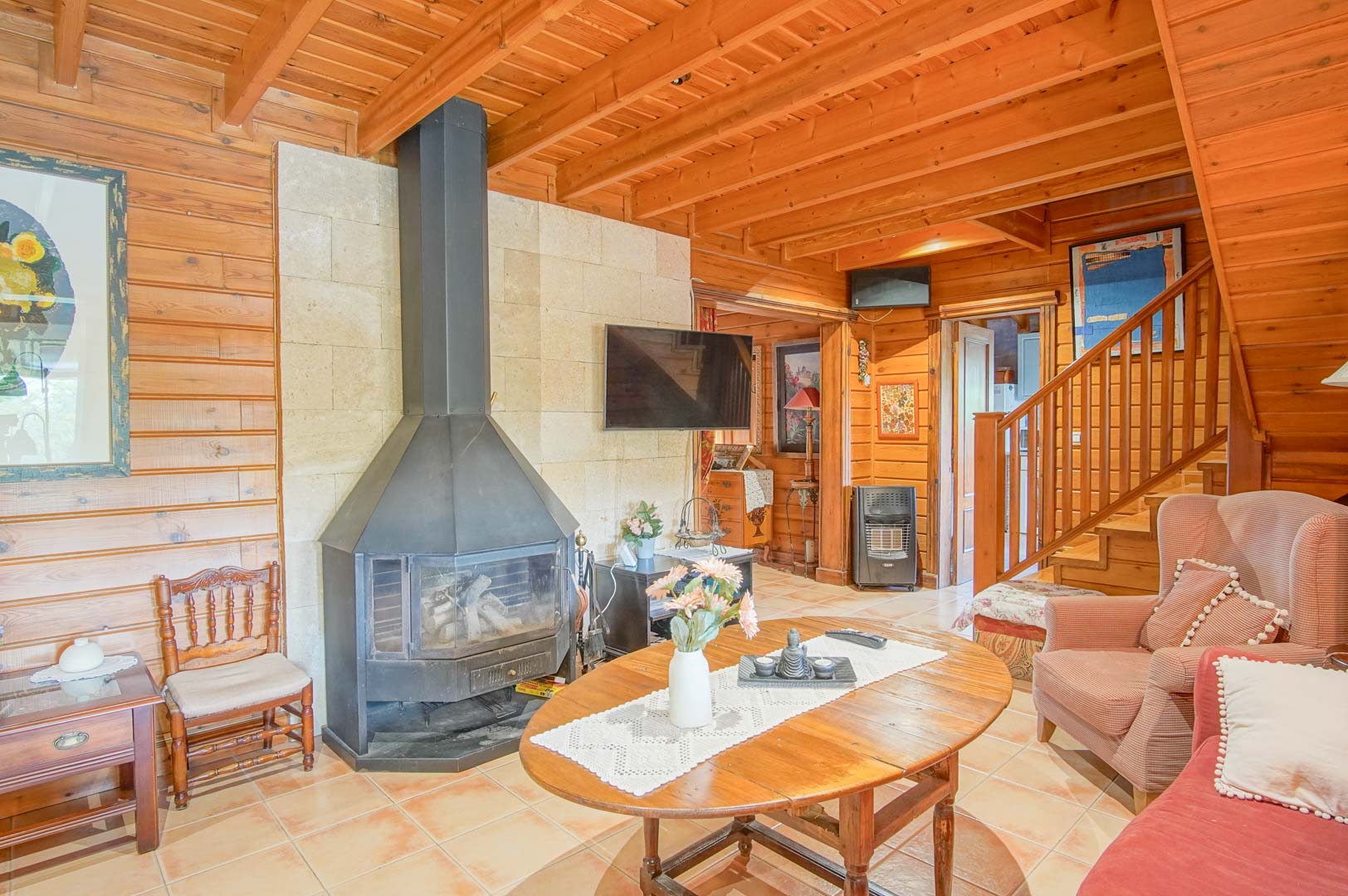 Rustic living area featuring Finnish pine walls and ceilings, a central black iron fireplace set against natural stone, and a handcrafted wooden staircase.