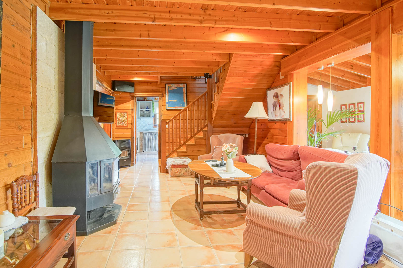 Rustic living room featuring Finnish pine walls and ceilings, a central black iron fireplace, and a wooden staircase leading to the upper floor.