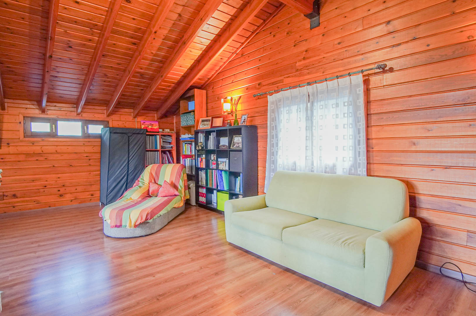 Spacious attic area fully lined with Finnish pine wood, featuring comfortable seating and bookshelves under a vaulted ceiling with exposed beams.