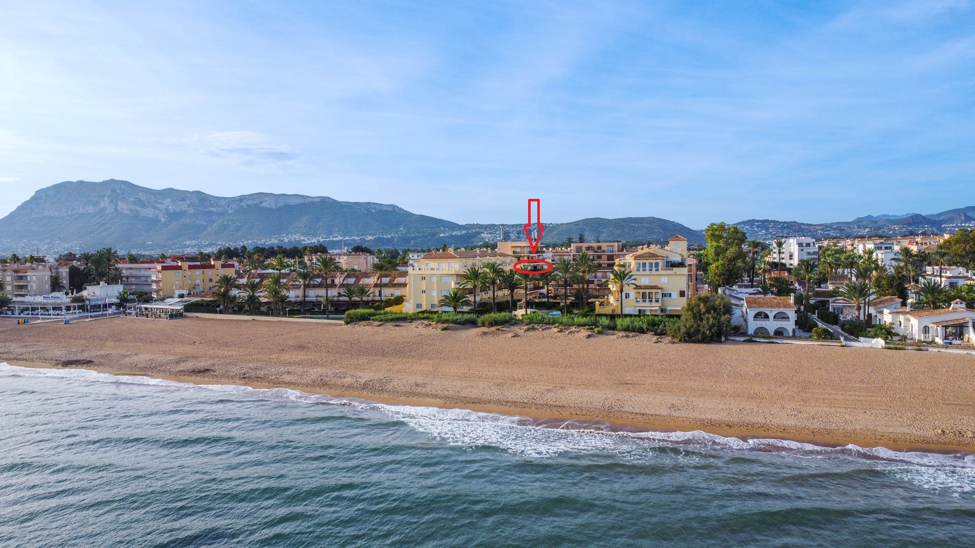 Aerial perspective of a beachfront apartment complex with a highlighted unit, featuring direct access to the sandy shore and scenic mountain views.