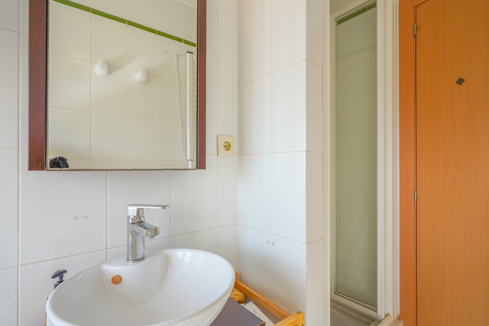Functional bathroom featuring a white ceramic basin, chrome faucet, and dark wood-framed mirror, adjacent to a shower with a frosted glass door.