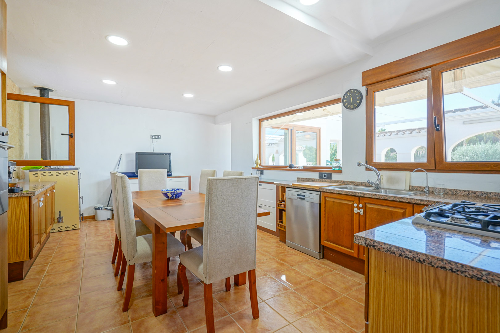 Fully equipped kitchen featuring granite countertops, wooden cabinetry, and an integrated dining area. It includes a traditional wood-burning oven and large windows.