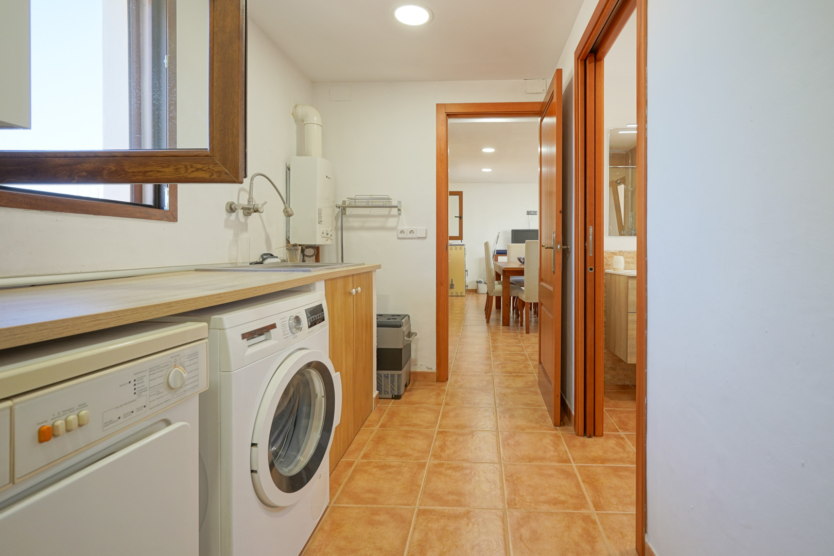 Functional laundry room featuring a wood-effect countertop, washing machine, and utility sink, with direct access to the dining area and bathroom.