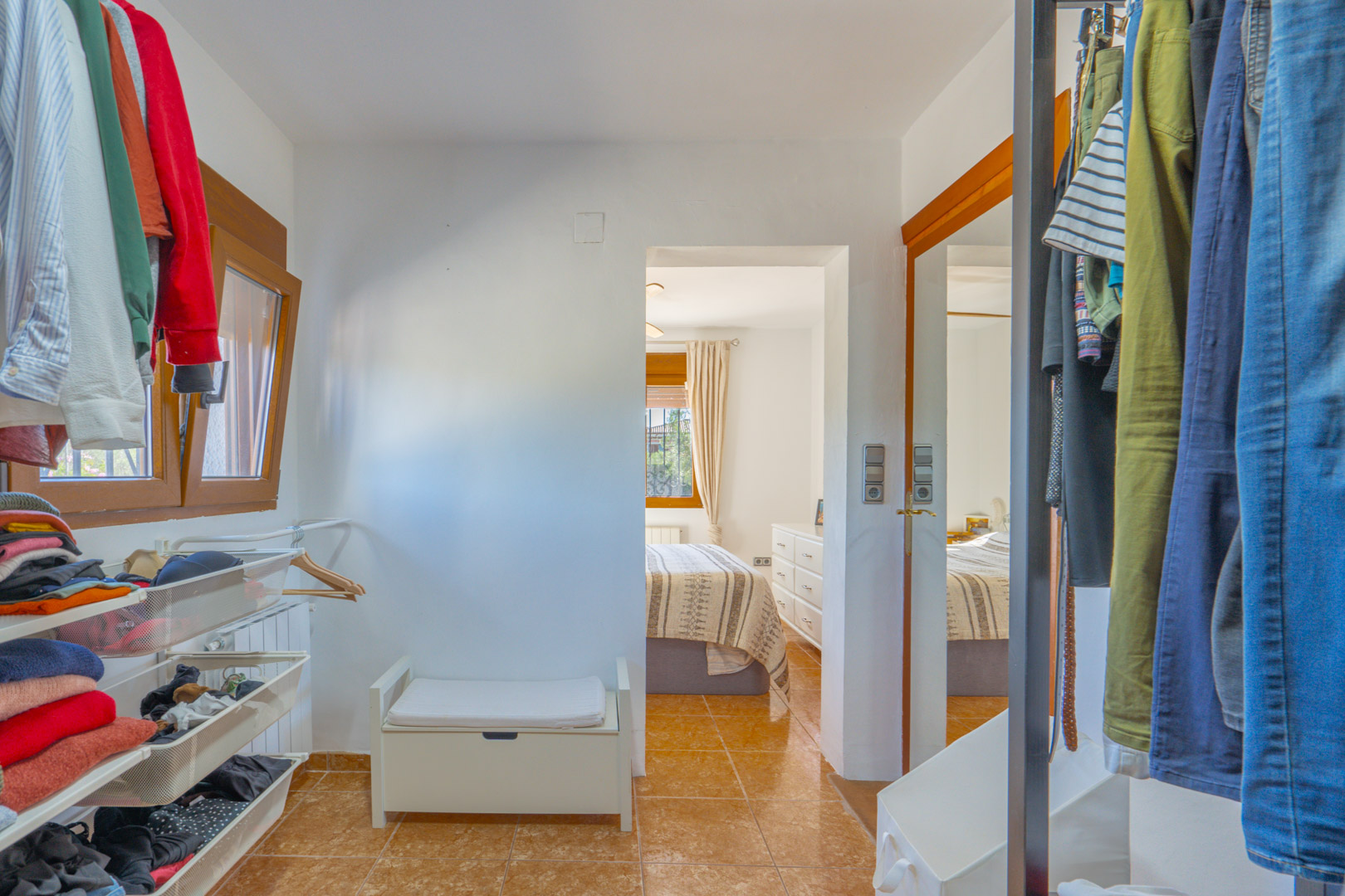 Functional walk-in closet featuring open shelving, mesh drawers, and hanging rails, directly connected to the bedroom with terracotta-style floor tiles.