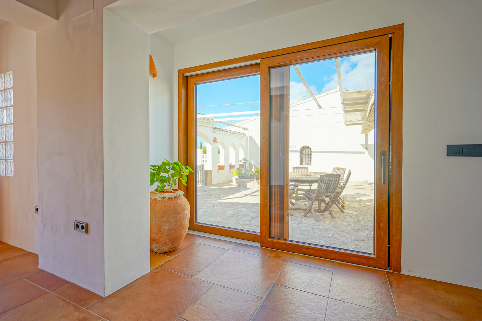 Large wood-framed sliding glass door connecting the terracotta-tiled interior to a stone-paved patio featuring an outdoor wooden dining set.