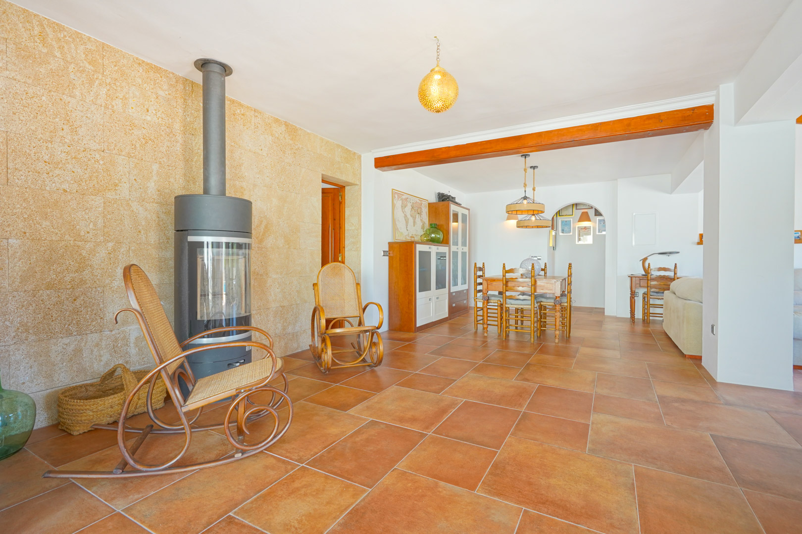 Living area featuring a modern wood-burning stove against a stone accent wall, terracotta tile flooring, and an integrated dining space.