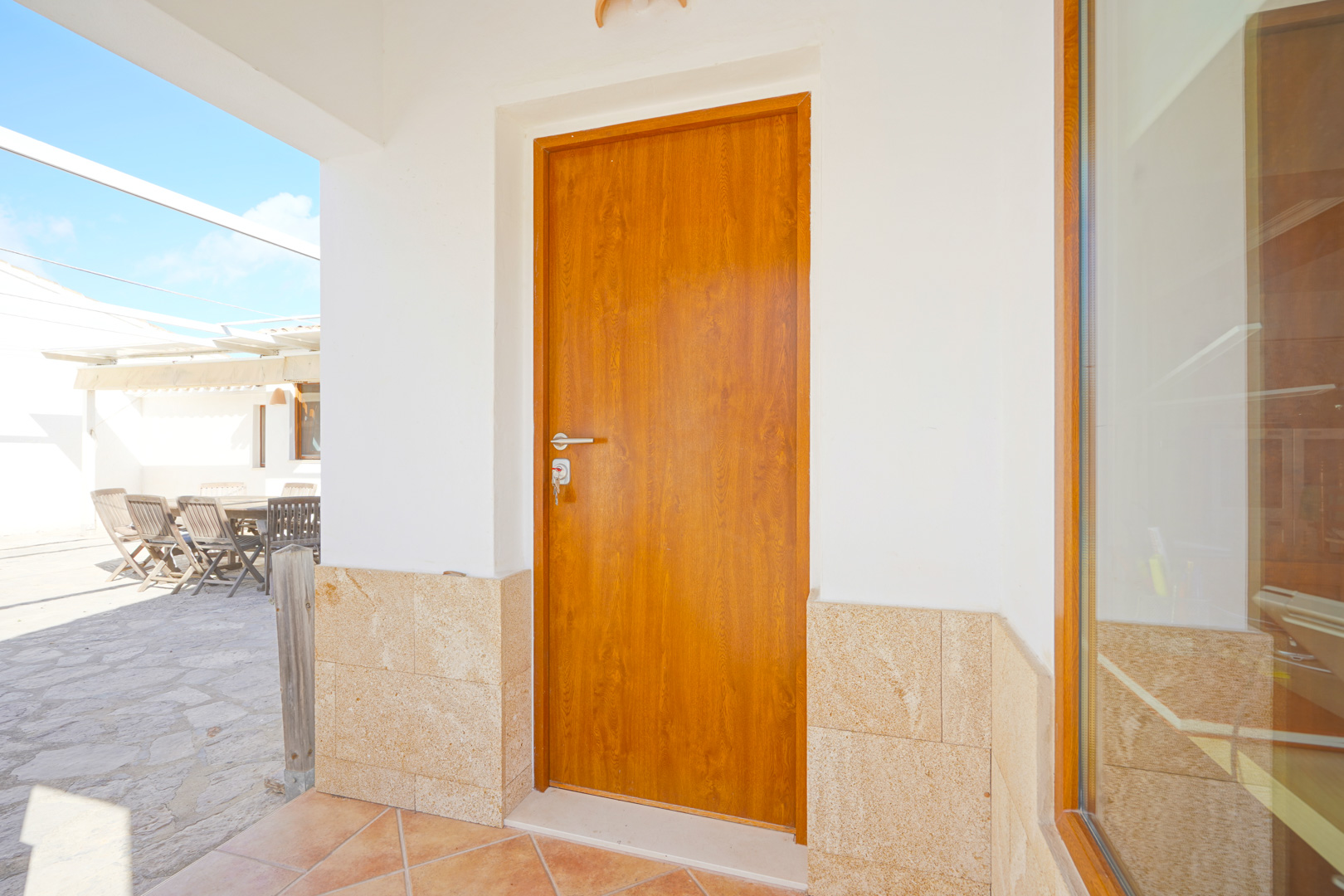 Main entrance featuring a wooden door, natural stone cladding, and terracotta flooring, opening onto a spacious sun terrace with outdoor dining.