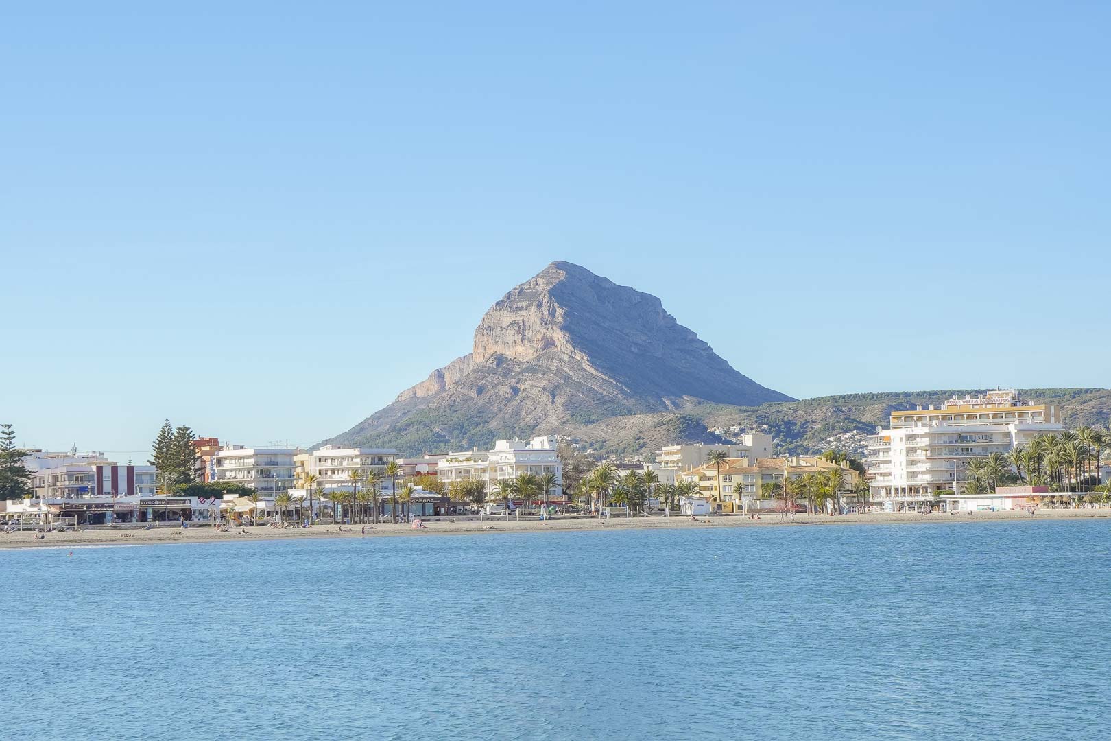 Panoramic view of Arenal beach in Jávea, featuring the iconic Montgó mountain backdrop and coastal architecture along the Mediterranean shore.