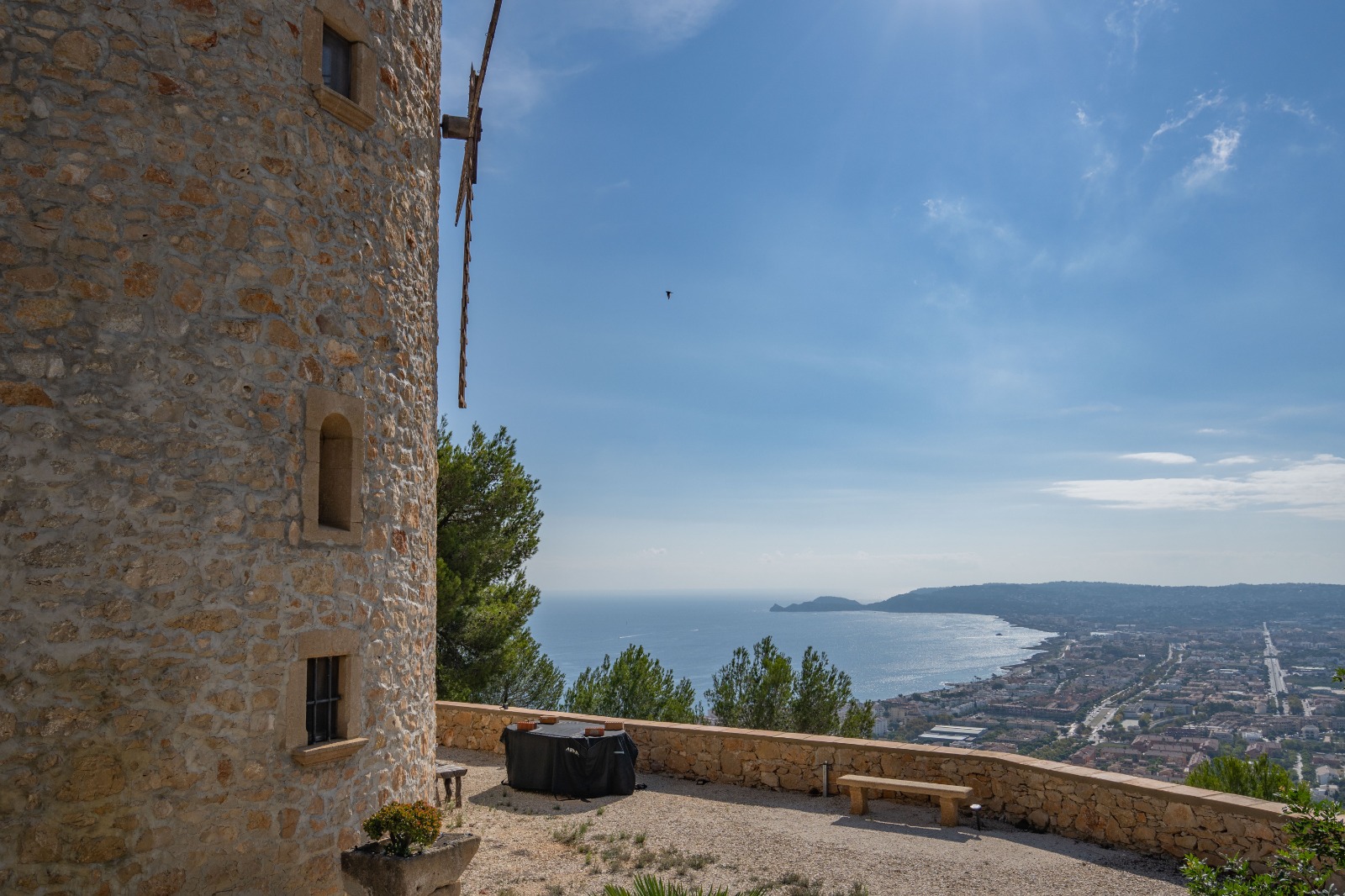 Panoramic views from the stone tower overlooking the Jávea bay and Mediterranean Sea, featuring a gravel terrace with a natural stone boundary wall.