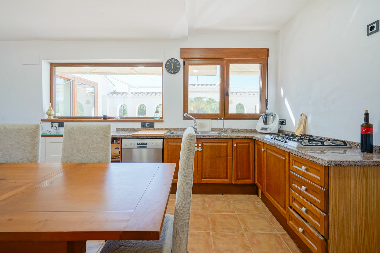Rustic kitchen featuring granite countertops, wooden cabinetry, and a dining area. Large windows provide natural light and views of the arched outdoor terrace.