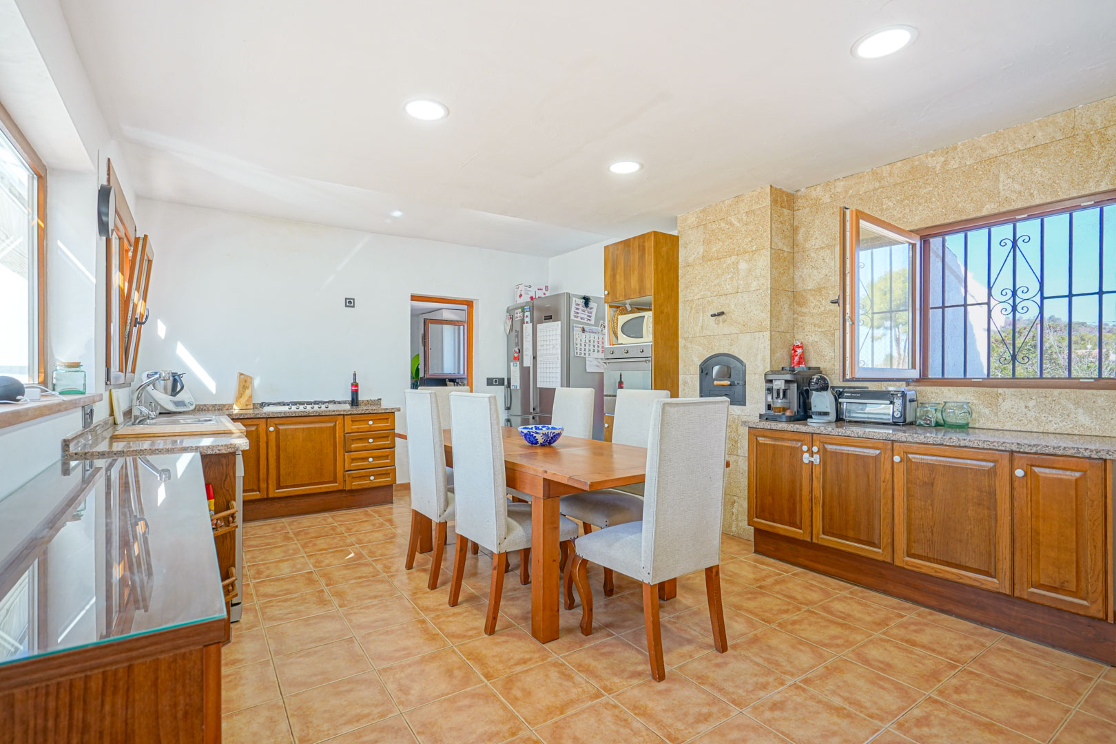 Rustic kitchen featuring wooden cabinetry, granite countertops, and a built-in wood-fired oven. The space includes a central dining area and tiled flooring.