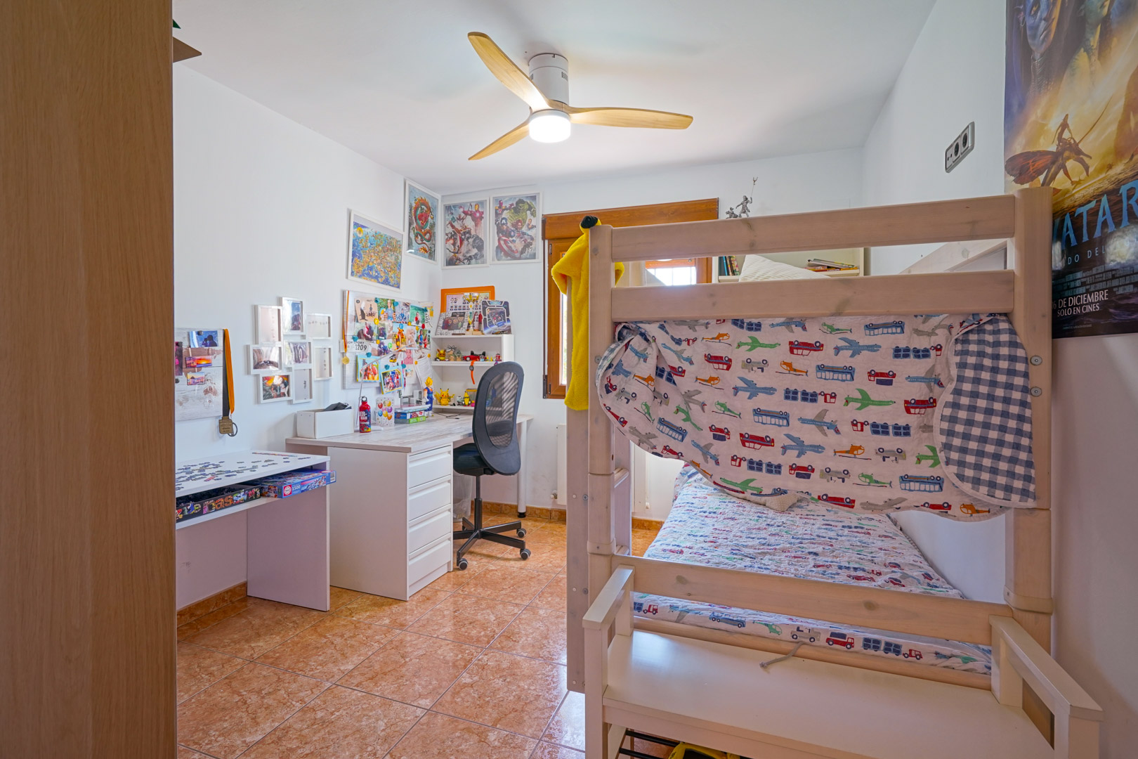 Youth bedroom featuring wooden bunk beds, a dedicated study desk, and a modern ceiling fan. The room is finished with ceramic floor tiles and receives ample natural light.