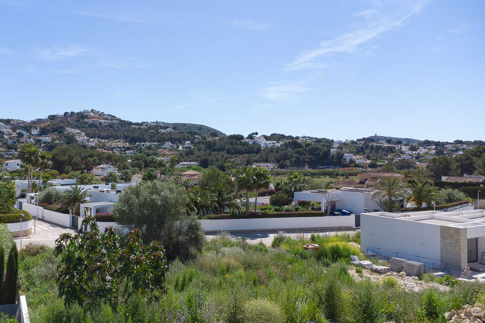 Elevated panoramic views of the Moraira residential area, showcasing modern white villas integrated into the Mediterranean landscape with lush greenery and rolling hills.