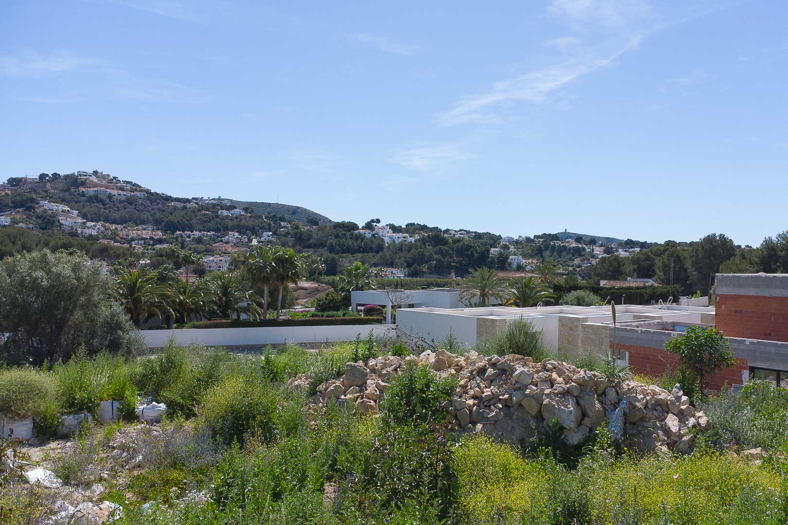 Elevated plot view overlooking the Moraira hills, featuring the natural landscape and neighboring villas under a clear blue sky.