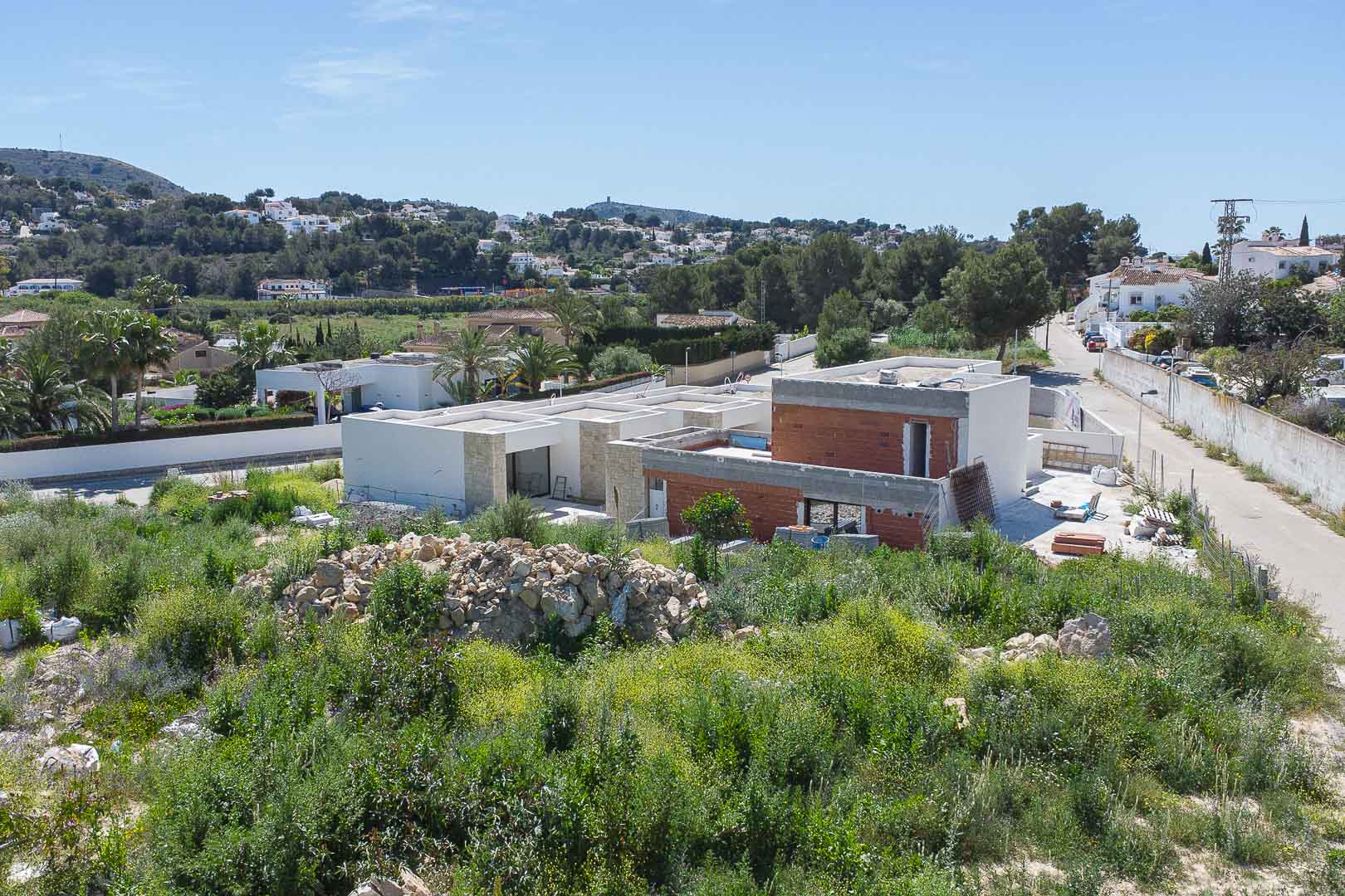 Exterior view of the villa under construction, showcasing modern architectural lines, natural stone cladding, and brickwork integrated into the Mediterranean landscape.
