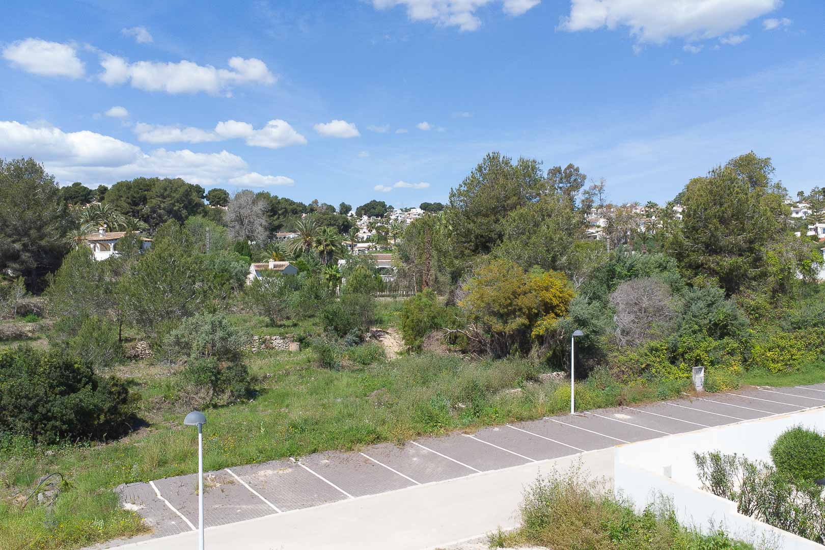 Panoramic views from the property overlooking the Mediterranean landscape, featuring lush vegetation, local architecture, and an outdoor parking area.