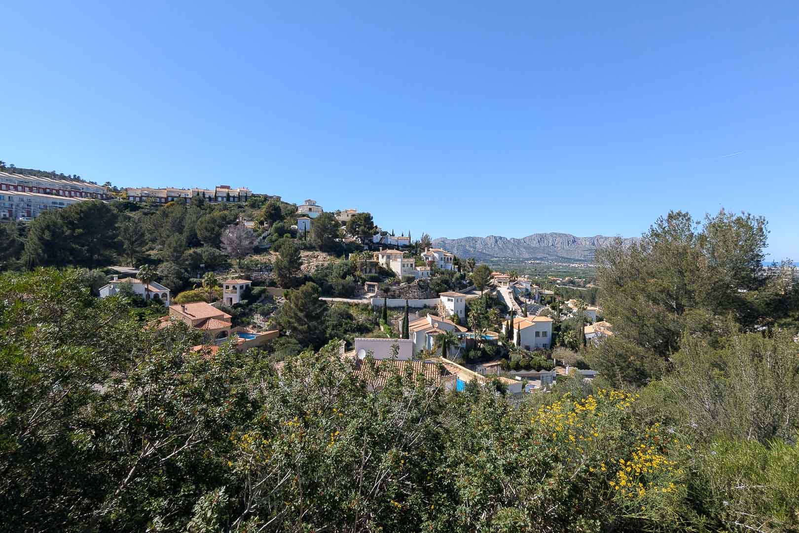 Panoramic view of the residential area featuring red-tiled houses and lush greenery under a clear blue sky.