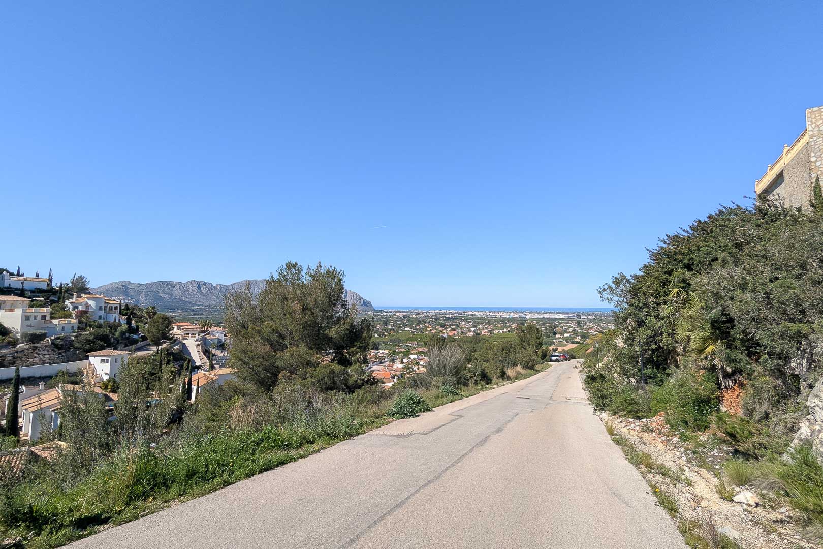 Villa access road with panoramic views of Pedreguer and the Mediterranean Sea on the horizon under a clear sky.