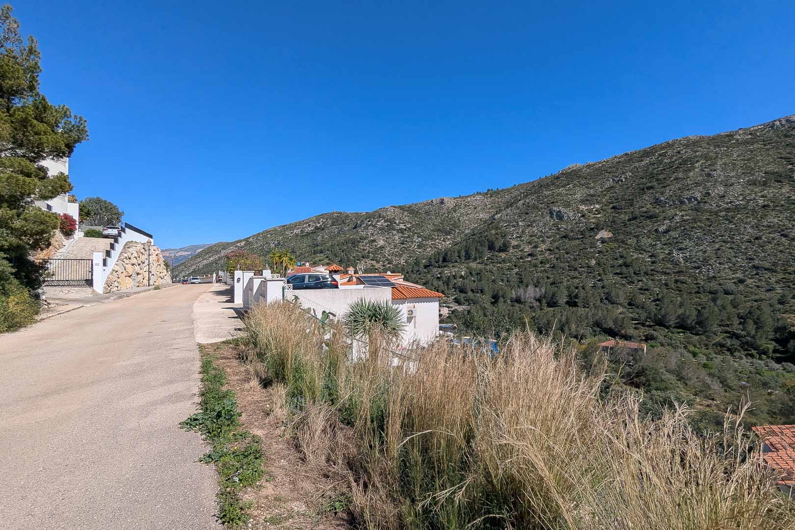 Exterior view of the villa from the access road, featuring roof-mounted solar panels and a panoramic backdrop of the Pedreguer mountains.
