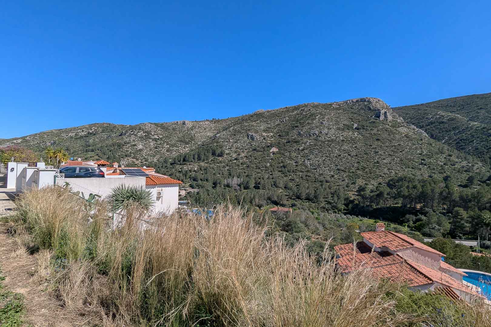 Panoramic mountain and valley views from the plot, showcasing the natural Mediterranean landscape and neighboring villas with terracotta roofs.