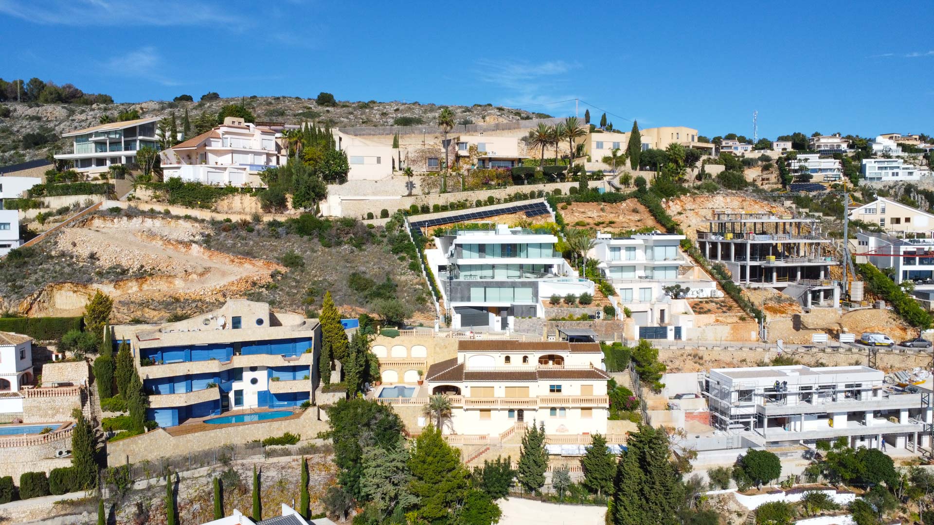Aerial view of the hillside villa in La Corona, showing its three-level traditional architecture with terracotta roofs and terraces integrated into the Mediterranean landscape.