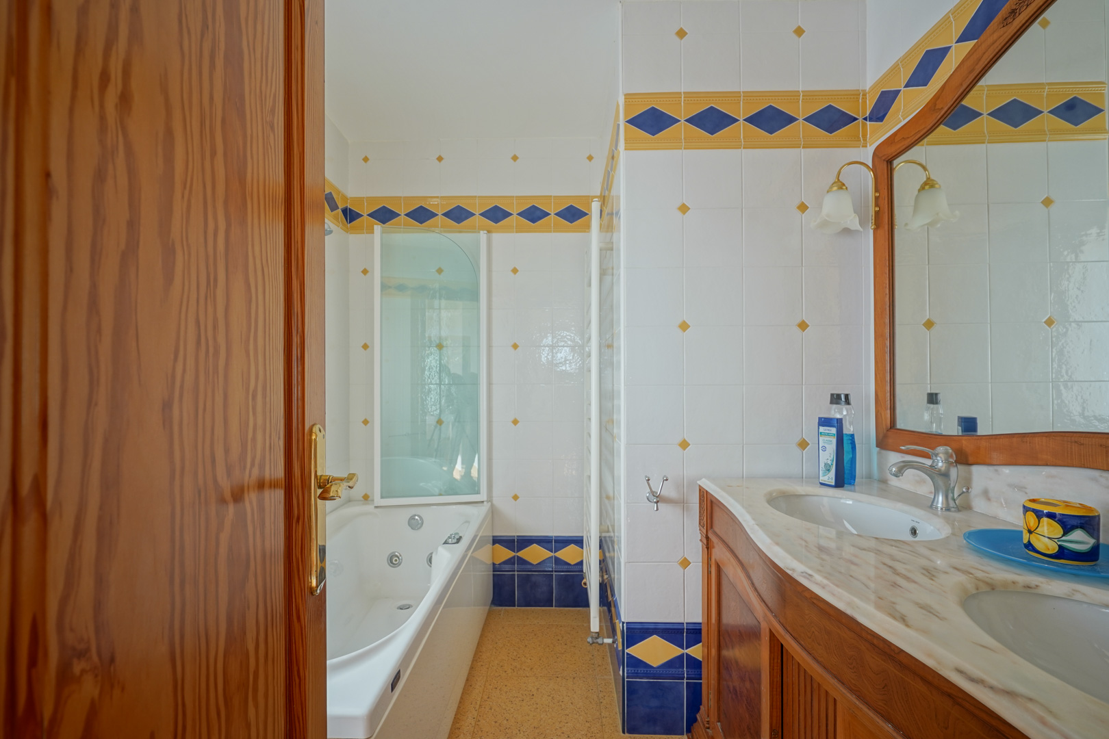 Bathroom featuring a double marble vanity, wooden cabinetry, and a hydromassage bathtub, finished with traditional blue and yellow patterned tile borders.