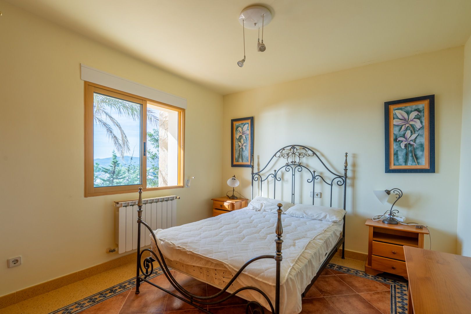 Bedroom featuring a wrought iron bed frame, terracotta tile flooring with decorative borders, and elevated views of the Mediterranean landscape.