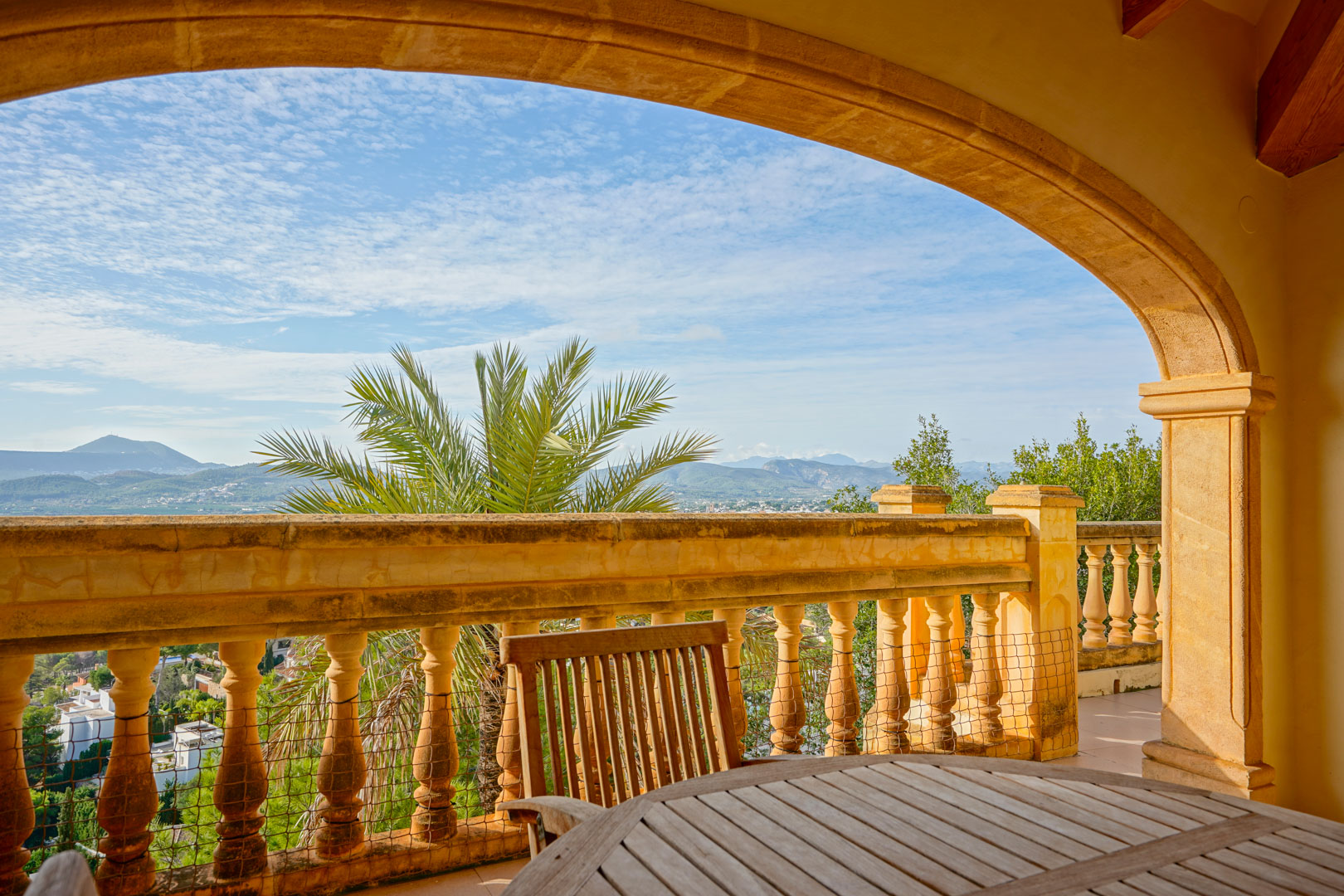 Covered terrace featuring a traditional stone arch and balustrade, overlooking the mountains and valley with wooden outdoor dining furniture.