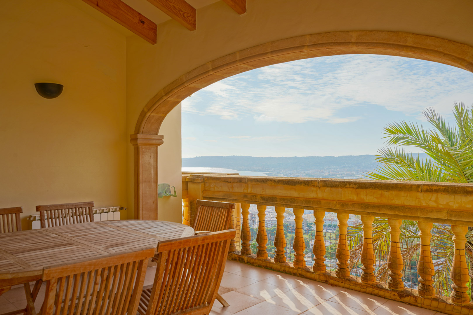 Covered terrace featuring a traditional stone arch, wooden beam ceiling, and a dining area overlooking the bay of Jávea and surrounding mountains.