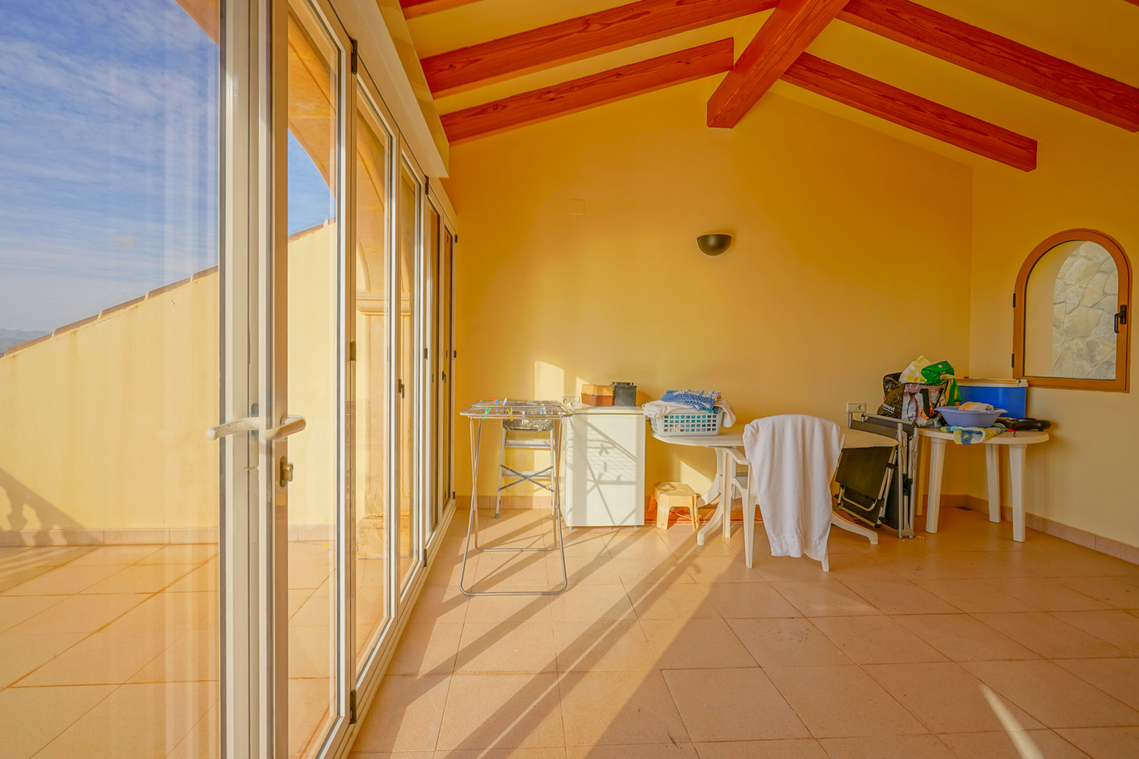 Enclosed sunroom featuring exposed wooden ceiling beams, tiled flooring, and floor-to-ceiling glass doors opening to the exterior.
