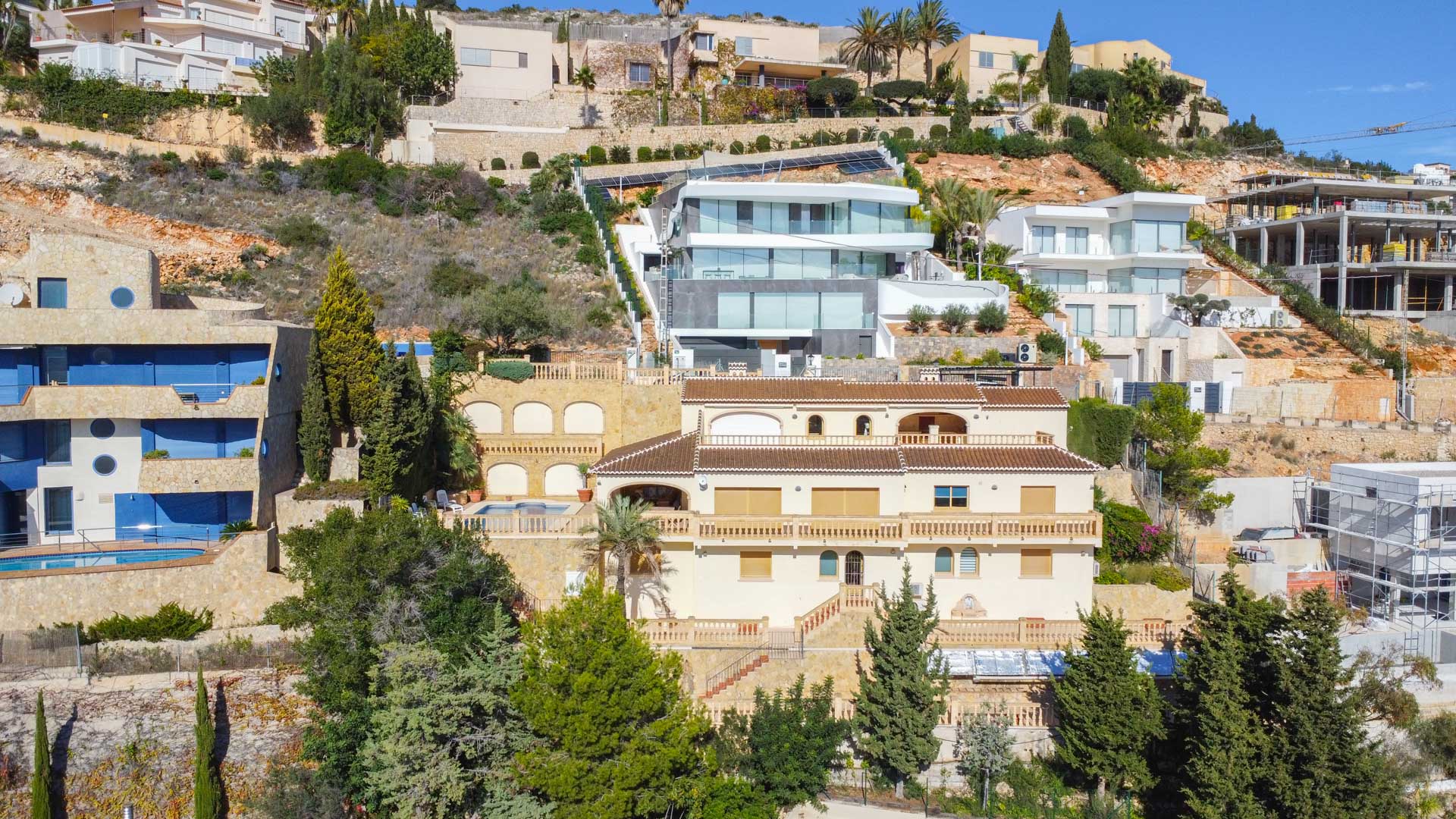 Exterior view of the traditional villa in La Corona, featuring a cream facade, terracotta tile roofs, and tiered terraces with balustrades built into the steep hillside.