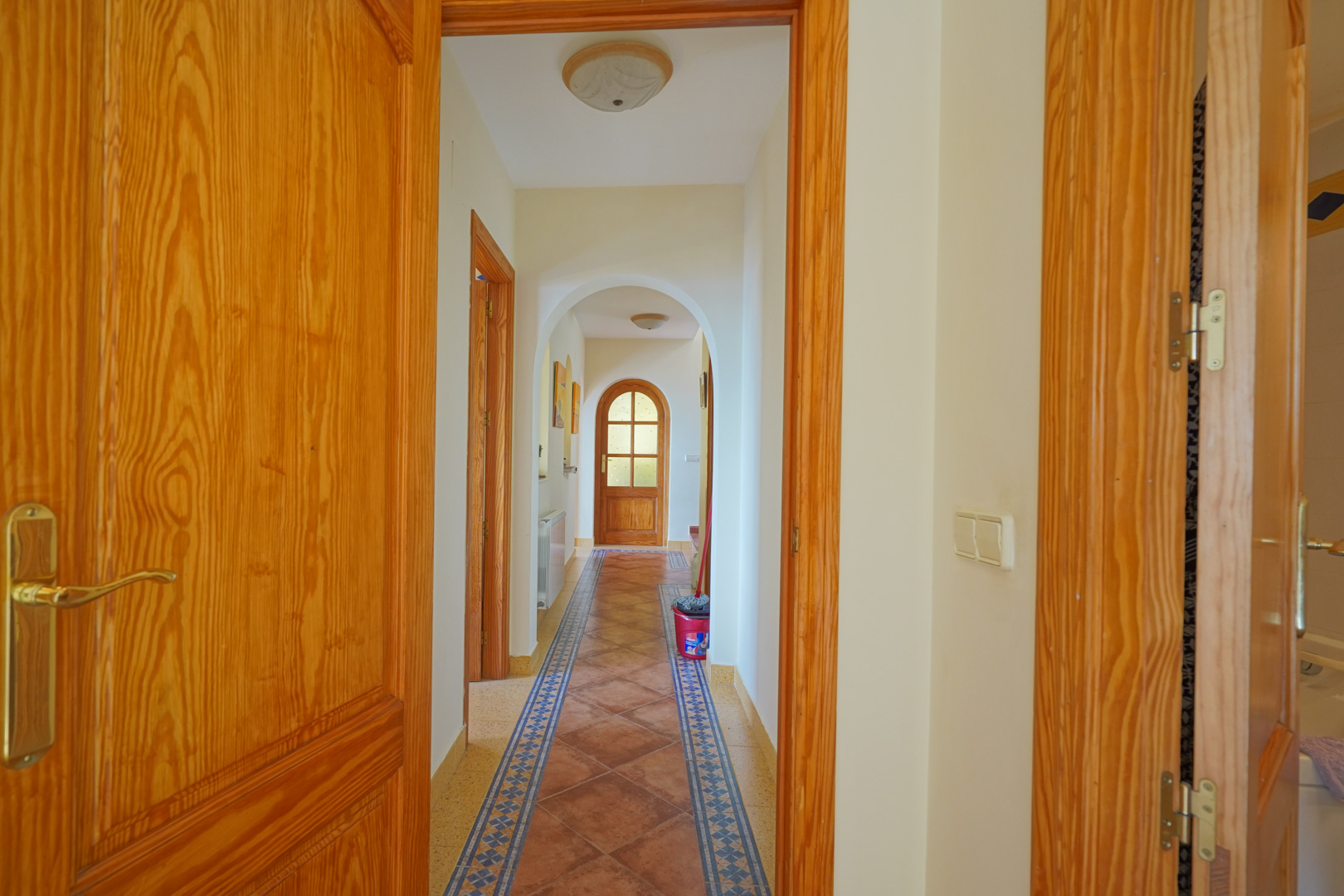 Hallway featuring traditional arched passages, terracotta floor tiles with decorative borders, and solid natural wood doors and frames.