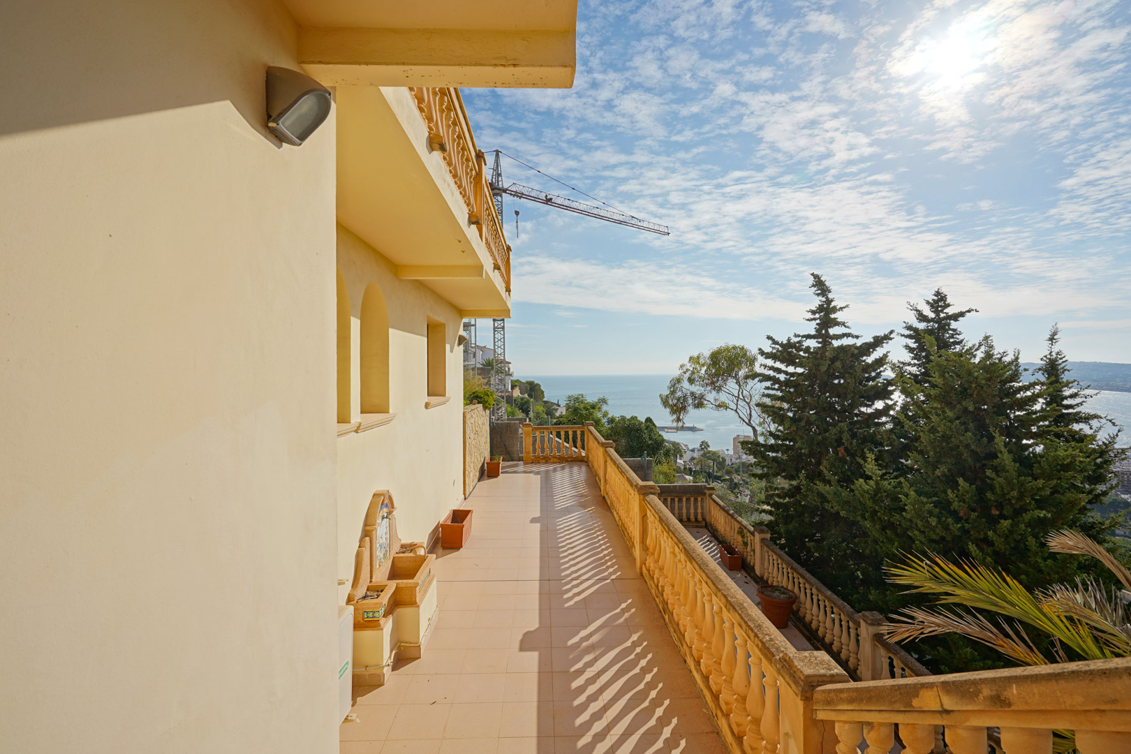 Long terrace featuring traditional stone balustrades, a decorative wall fountain, and expansive views over the Mediterranean Sea and Javea coastline.