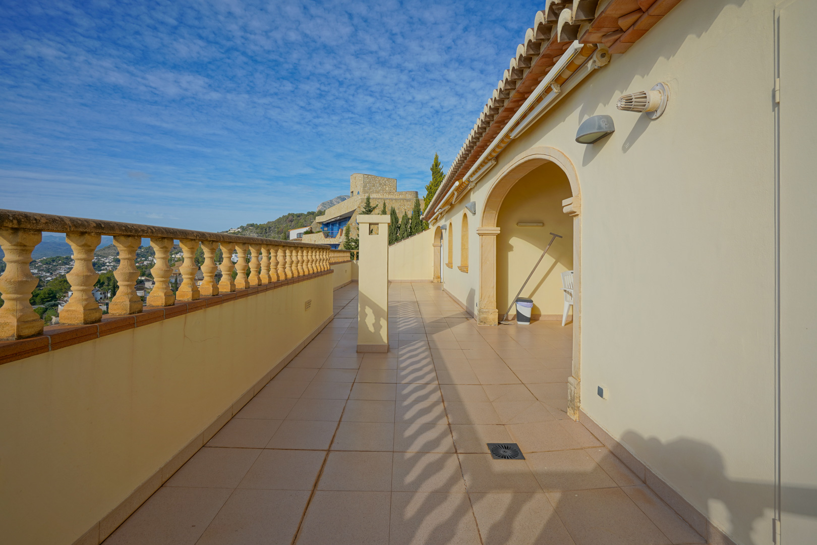 Long terrace featuring traditional stone balustrades, ceramic tiling, and arched architectural details overlooking the surrounding Mediterranean landscape and valley.