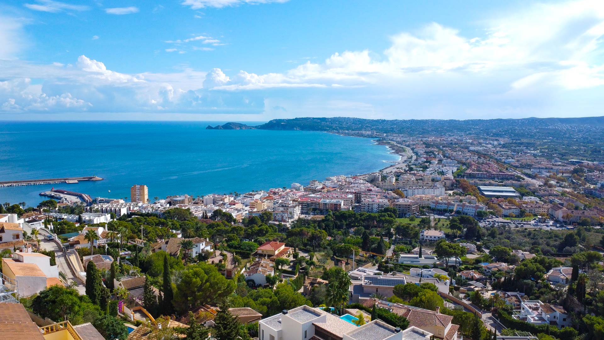 Panoramic aerial view from La Corona overlooking the Bay of Jávea, the local harbor, and the distant Cap Negre headland.
